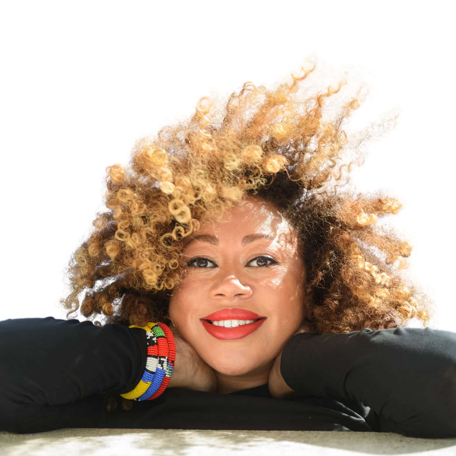 Picture of Ithalia with voluminous curly hair wearing black clothing and colorful beaded bracelets against white background.